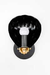 A black and gold wall sconce designed in a traditional chinoiserie-inspired style, featuring a shell-shaped black metal shade and an exposed round light bulb, mounted on an ornate gold base with intricate detailing.