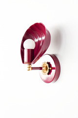 Seen in profile, the Coquille Sconce shows off its construction: a fluted shell shade in glossy black cherry powder coat, tilted forward on a color-matched arm with a brass ball detail and ornate fluted rosette. The exposed globe bulb nestles into the curve of the shell. Vintage-inspired lighting with real presence for powder rooms, colorful bathrooms, and bedrooms in grandmillennial and collected traditional homes.