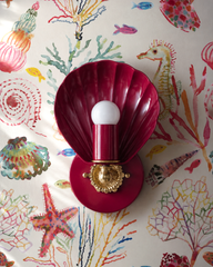 Seahorses, starfish, coral, and scallops drift across this watercolor sea life wallpaper in rainbow washes, and a real scallop joins the scene. The Coquille Sconce in Black Cherry picks up the deepest reds in the print, its glossy fluted shell and cast brass rosette anchoring all that painterly color. A playful pairing for colorful coastal bathrooms, kids bathrooms, and whimsical powder rooms where the wallpaper tells the story and the lighting plays along.