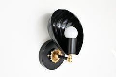 A black and gold wall sconce designed in a traditional chinoiserie-inspired style, featuring a shell-shaped black metal shade and an exposed round light bulb, mounted on an ornate gold base with intricate detailing.