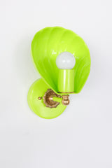 Front-facing product image of a bold chartreuse Coquille sconce with a glossy shell silhouette, white globe bulb, matching chartreuse mount, and warm brass accent details. The design has a playful, high-design look that suits colorful coastal interiors, chic pool bathrooms, boutique hotel suites, and resort-inspired spaces that lean British West Indies or elevated tropical rather than kitschy beach decor. Ideal for keywords like shell wall sconce, chartreuse bathroom light, statement coastal lighting, tropi