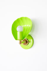 Angled product photo of the Coquille shell sconce in a vivid chartreuse finish, highlighting its glossy shell-shaped shade, white globe bulb, round backplate, and warm brass arm with decorative floral hardware. This colorful wall sconce feels both whimsical and elevated, perfect for a pool house bathroom, a stylish powder room, a boutique hotel corridor, or a tropical-inspired bedroom with a polished island-luxury aesthetic. Great for searches related to chartreuse wall lights, shell sconces, beach house li