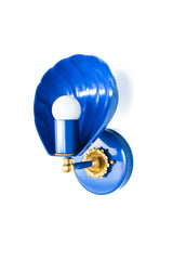 Side angle product photo of a Mediterranean Blue shell sconce showing the depth of the scalloped shade, the glossy blue finish, the round wall plate, and the brass flower rosette behind the bulb. The compact scale and curved ceramic-like shell shape make it a good decorative wall light for small bathrooms, colorful powder rooms, coastal bedrooms, kids bathrooms, beach house hallways, and blue and brass interiors. It has a little vintage glamour, a little seaside energy, and a lot of personality.