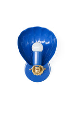 Studio product photo of the Mediterranean Blue Coquille Sconce, a bright blue wall light with a shell-inspired scalloped shade, brass accents, and a white globe bulb. The shape gives it a soft coastal feel, while the bold blue finish makes it more fun and design-forward than a plain bathroom sconce. Use this style for bathroom vanity lighting, powder room sconces, nautical guest bathrooms, colorful kids baths, cottage hallways, bedside lighting, or any space that needs a small statement light with charm.