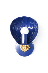 Studio product photo of the Navy Coquille Sconce, a shell-shaped wall light with a glossy navy scallop shade, round navy backplate, brass flower rosette, and white globe bulb. The curved shell shade gives it coastal, Art Deco, and vintage-inspired character without feeling kitschy. This small statement sconce works well for bathroom vanity lighting, powder rooms, bedside lighting, hallways, coastal homes, blue and white interiors, nautical decor, and colorful grandmillennial spaces.