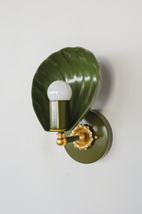 From this angle, the Coquille Sconce shows how the fluting wraps the outer shell like a real scallop. The deep olive powder coat covers shade, arm, and backplate in one mossy, glossy sweep, while the cast brass rosette and ball detail catch the light below the exposed globe bulb. Earthy, sculptural lighting for English cottage bathrooms, moody powder rooms, and collected traditional homes drawn to green with depth.