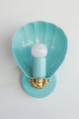 Shell-shaped wall sconce light fixture in a light aqua blue color with cast brass details.  Nancy Meyers aesthetic that also works with coastal or chinoiserie styled interiors.  Powdercoated steel with brass accents. Perfect wall sconce for powder rooms, bathrooms, and more.  Adds a little bit of fun whimsy with the nautical shell shape of the sconce.