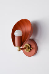 Angled studio image of the Terra Cotta Coquille Sconce, showcasing the dimensional shell-shaped shade and its curved, fluted form. The terra cotta finish gives the fixture a warm earthy tone, while the brass rosette detail and brass accent hardware add a vintage-inspired touch. This decorative wall sconce blends sculptural lighting, coastal style, romantic decor, and artful statement design, making it ideal for bathrooms, hallways, bedrooms, or eclectic interiors.