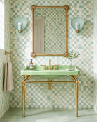 Coastal green bathroom with mint and cream square wall tile, soft green floor tile, a pale green console sink, and warm brass legs, faucet, towel ring, and mirror frame. A pair of Mint and Brass Coquille sconces flank the mirror, adding shell-shaped wall lighting that feels coastal, Art Deco, and a little grandmillennial without going kitschy. The glossy scallop shades and brass details make these strong bathroom vanity lights for a beach house bathroom, powder room, spa bath, colorful kids bathroom, or any