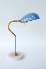 Coquille desk lamp in pastel hydrangea blue with a brass curved arm and solid marble base, featuring an Art Deco-inspired shell shade. This stylish midcentury modern lamp adds a coastal vibe and pop of color to any desk, bedside table, or reading nook, perfect for eclectic and contemporary decor styles.