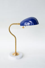 Coquille desk lamp in rich Navy Blue with a brass curved arm and solid white marble base, featuring an Art Deco-inspired shell-shaped shade. Ideal for adding a pop of color and midcentury modern charm to desks, bedside tables, or reading nooks in coastal and eclectic decor styles.