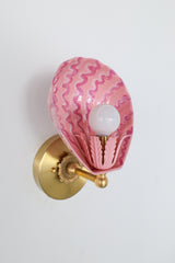 Angled side view of handmade pink Coquille sconce with glossy blush powder-coated steel shell shade and layered squiggly brushstrokes in fuchsia and rose tones, mounted on a round solid brass backplate – artistic wall lighting for vintage-inspired powder rooms or colorful interiors