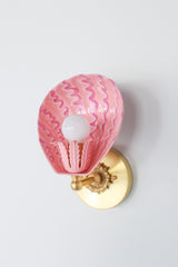 Angled side view of handmade pink Coquille sconce with glossy blush powder-coated steel shell shade and layered squiggly brushstrokes in fuchsia and rose tones, mounted on a round solid brass backplate – artistic wall lighting for vintage-inspired powder rooms or colorful interiors