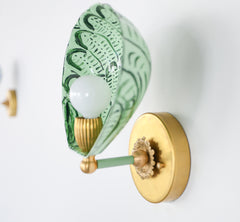 Side angle of the one-of-a-kind Coquille wall sconce with a scalloped shell design hand-painted in shades of green, including vista green accents on powder-coated steel, mounted with a vintage-style brass backplate and socket, perfect for maximalist or Art Deco wall lighting in bathrooms, hallways, or powder rooms
