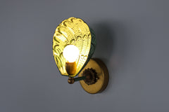 Side profile of the handmade Coquille sconce with a powder-coated steel shell shade in vibrant layered greens, including vista green highlights, set against a pastel blue wall with vintage-inspired brass mounting hardware, offering a bold yet refined lighting solution for maximalist interiors