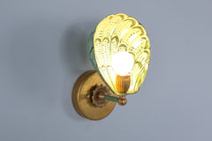 Side profile of the handmade Coquille sconce with a powder-coated steel shell shade in vibrant layered greens, including vista green highlights, set against a pastel blue wall with vintage-inspired brass mounting hardware, offering a bold yet refined lighting solution for maximalist interiors
