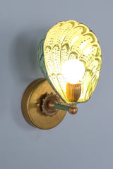 Close-up detail of the green hand-painted Coquille sconce with botanical-inspired brushstrokes on a powder-coated steel scallop-shaped shade, sealed in a clear coat for durability, paired with fluted brass hardware and a round glowing bulb, designed for use in colorful and creative interior lighting plans