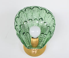 Front view of the Coquille wall sconce featuring a hand-painted shell-shaped shade in layered greens including vista green and olive, crafted from powder-coated steel with a sealed clear coat, paired with a glowing bulb and brass hardware, designed and handmade in New Orleans for eclectic, coastal-inspired interiors