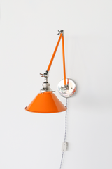 This angle shows off the engineering behind the Cora Sconce: a double-jointed chrome arm with exposed wingnut hardware lets the orange cone shade swing and tilt to direct light exactly where it's needed. Unlit here, the glossy orange finish and polished chrome joints stand out on their own, a strong choice for anyone comparing adjustable wall sconces for a bedroom or home office.