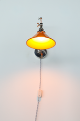 Switched on, the Cora Sconce shows exactly why it works as a reading light: the glossy orange cone shade glows warm from within, while the chrome articulating arm and exposed wingnut joints keep the whole fixture adjustable and industrial in the best way. A great pick for anyone searching adjustable wall sconce bedroom or retro task lighting with real personality.