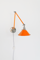 An orange articulating wall sconce with a two-part swing arm, glossy cone shade, and nickel wing nut joints, shown with the arm extended out from the wall. It plugs in with a gray twisted cloth cord and inline switch, so you can mount it without hardwiring. Pull it out over a bed or desk for reading and fold it back when you are done. Orange and nickel on a white wall read as clean and graphic, so it suits mid century modern, industrial, and renter friendly bedrooms.