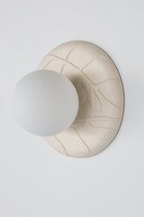 Studio photo of Lierre ceramic wall sconce in unglazed cream porcelain, raised leaf relief plate with matte white globe, sculptural lighting for organic modern and grand millennial interiors.