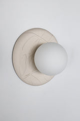 Studio photo of Lierre ceramic wall sconce in unglazed cream porcelain, raised leaf relief plate with matte white globe, sculptural lighting for organic modern and grand millennial interiors.