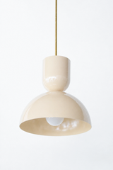 Cream is the warm neutral that softens a kitchen without going flat, and this Taeuber pendant keeps it from ever reading plain. The two-part silhouette stacks a rounded cup over a wide domed bell, all finished in a glossy warm ivory with a brass stem, shown here lit and glowing. The soft tone is warmer than a stark white, so it plays beautifully against wood, marble, aged brass, and any color you bring in elsewhere. Versatile over an island, breakfast nook, or sink, it brings a gentle glow without competing
