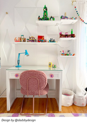 White desk styled in a teenage girls room with pink daisy drawer pulls, a pink boucle chair, glass desktop, white floating shelves, geometric wall treatment, and cheerful colorful decor. Pretty feminine study space with flower drawer knobs, girls desk inspiration, playful bedroom storage, pastel kids room design, cute teen room furniture, eclectic girl bedroom decor, and whimsical hardware that makes a simple white desk feel custom and fun.