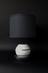 The Delta Lamp by Sazerac Stitches is a modern and elegant piece featuring a speckled ceramic base, a black linen drum shade, and a smooth black marble base. Perfect for adding minimalist sophistication to any space.