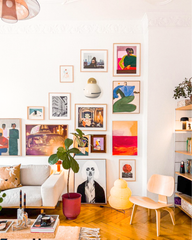 Delta ceramic globe sconce with brass cap and black accent stripe centered within a bold European-style gallery wall of colorful modern art, hung on crisp white plaster walls above a light sofa, sculptural floor lamp, potted fiddle-leaf fig in a red planter, low coffee table, and blond wood chair, creating an eclectic, art-forward living room vignette.