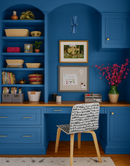 A denim blue Dryades Sconce is mounted above framed art in a custom home office with fully painted royal blue built-ins and a natural wood desktop. Woven storage baskets and playful pops of color—like pink flowers and a child’s drawing—lend warmth to the highly coordinated, monochromatic color scheme. This sconce adds a subtle sculptural touch to a workspace designed for both creativity and order. Ideal for customers searching for unique accent lighting in a colorful, cohesive home office or study.