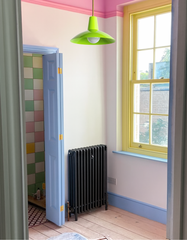 Chartreuse Bruxelles Pendant Light with brass stem, styled in a playful English-inspired interior with pastel colorblocked trim and bold details. Small hallway with pink ceiling and crown molding, sky blue door and trim, sunny yellow window frame, and black cast iron radiator, leading into a bathroom with multicolored checkerboard tile. Handmade modern pendant lighting by Sazerac Stitches, perfect for eclectic interiors, colorful homes, and bold pastel design schemes.