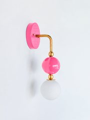 A statement wall sconce for rooms that lead with color and personality. This angle of the Ida sconce puts the bold round doll-pink backplate front and center, with a brass arm curving down to a glossy pink sphere and frosted glass globe. Glossy, saturated, and unapologetically pink, it's a playful pick for colorful bathrooms, powder rooms, girls' bedrooms, and maximalist spaces that want one joyful, standout detail.