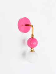 Colorful vanity lighting that brings a bathroom or powder room to life. Seen in profile, the Ida sconce shows off its curved brass arm reaching from a glossy doll-pink backplate down to a stacked pink sphere and frosted glass globe. The side view highlights the brass ball detailing and the projection off the wall. A bold, feminine choice for grandmillennial, maximalist, and colorful traditional homes.