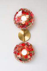 Modern two light wall sconce with brass hardware and red flowers. Features resin-encapsulated pink & purple flowers with greenery, ferns, and leaves.  Adds a real-like nature theme to any interior design project.  Called the Botanico Sconce by Sazerac Stitches. Features red flowers with greenery