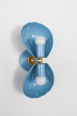A double wall sconce with two fluted, shell-form shades in a dusty slate blue, connected by an ornate brass floral rosette. A strong option for coastal bathroom lighting, Southern traditional powder rooms, or grandmillennial decor that wants a scalloped, sculptural fixture in a softer, more muted blue than a standard bright colorway.