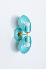 Double Coquille sconce in poolside turquoise with brass hardware, shown opened flat with both fluted shell shades splayed outward, revealing the full brass floral rosette and both cylindrical sockets, unlit with exposed white bulbs.