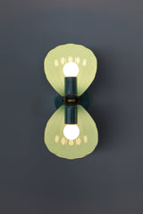 A closer, straight-on look at the poolside teal Double Coquille sconce, showing the scalloped, fluted shell shades and the ornate brass floral rosette at the center mount. Both bulbs lit, casting a warm glow through the shades. A coastal or grandmillennial pick for anyone tired of plain glass globe sconces and wanting a fixture with real texture.