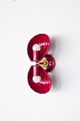 Double Coquille wall sconce in glossy Black Cherry, a deep wine-red finish that reads like lacquered candy. Two sculptural scallop shells frame the bulbs and create a symmetrical, Art Deco silhouette, with warm brass details at the center for a hint of vintage glamour. Shot straight-on against a clean white background, this image is ideal for searches like shell sconce, scallop shell wall light, coastal glam lighting, boutique hotel bathroom sconce, statement powder room lighting, and colorful brass wall sc