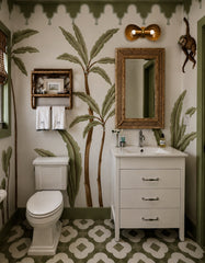 Tropical powder room styled with hand painted palm mural wallpaper, deep green trim, and a geometric patterned tile floor. Above a woven rattan mirror and crisp white vanity, the Double Coquille wall sconce in rich fudge brown with warm brass details adds sculptural shell-inspired charm. This look is perfect for coastal bathroom lighting, Palm Beach style decor, grandmillennial interiors, and boho modern powder room design, delivering soft vanity light with a bold, playful pop of color.