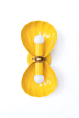 A double wall sconce built from two fluted, shell-form shades in a bright, confident golden yellow, joined by an ornate brass floral rosette. The scalloped shape has real coastal roots but doesn't read beachy, which means it works just as well in an English cottage kitchen, a grandmillennial breakfast nook layered with gingham and antiques, or a fully maximalist eclectic room that leans into color instead of avoiding it. Pair it with butter yellow cabinetry for a matched moment, or let it stand out as the o