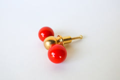 A double-ball cabinet knob pairing two glossy red spheres with a polished brass ball at the center, shown at an angle to show its full shape. A confident, saturated pick for a bold kitchen or any cabinetry that wants real color and presence.