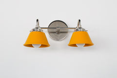Straight-on view of the Double Kelly Sconce in matte mustard and chrome featuring two compact cone shades on a polished chrome arm and round backplate. This popular small bathroom wall sconce is designed for over-mirror lighting, double sink vanity layouts, and colorful eclectic bathrooms needing a bold yellow statement light with a clean modern profile.