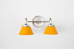 Straight-on view of the Double Kelly Sconce in matte mustard and chrome featuring two compact cone shades on a polished chrome arm and round backplate. This popular small bathroom wall sconce is designed for over-mirror lighting, double sink vanity layouts, and colorful eclectic bathrooms needing a bold yellow statement light with a clean modern profile.
