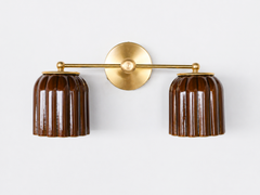 Handmade Double Marcella Sconce in chicory brown glazed ceramic — two fluted, scalloped shades on a brass arm and round backplate. Celadon-style glazing at its best: the glaze pools espresso-dark in the flutes and breaks to honeyed amber on the ribs, so it reads as a rich tortoiseshell neutral that turns jewel-toned in the light, not flat brown. Deco-inspired ribbing keeps it feminine and architectural. Layers beautifully with wood, cream, and leather. Shop handmade ceramic sconces, glazed brown wall lighti