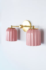Side angle photo of the Double Marcella ceramic wall sconce showing glossy blush pink ribbed ceramic shades and a brass arm and backplate, a statement bathroom light for chinoiserie inspired spaces, pastel interiors, and classic traditional rooms that need a fun unexpected hint of color