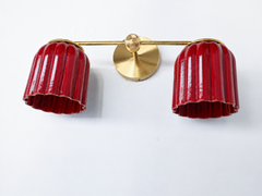 Handmade Double Marcella Sconce in jasper red glazed ceramic — two fluted, scalloped shades on a slim brass arm and round backplate. The glossy oxblood glaze pools richer and darker in the flutes and catches light on the raised ribs, so the color reads as a deep jewel-red that shifts from bright cherry to smoky garnet as it curves. Deco-inspired ribbing keeps the silhouette feminine and architectural, while brass warms the whole piece. This small-batch ceramic sconce makes a confident statement flanking a m