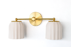 Handmade Double Marcella Sconce in a warm, unglazed cream that works like a soft neutral with a sculptural edge. The bare ceramic has a matte, chalky finish that reads as gentle ivory in daylight and warms further under bulbs, so it settles into any palette while the fluted Deco ribbing and brass keep it from feeling plain. A quiet fixture that goes with everything — white, wood, or color. Shop handmade ceramic sconces, unglazed cream wall lighting, neutral fluted sconces, and warm Art Deco bathroom lightin