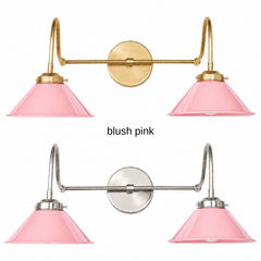 A pale pink two-light gooseneck wall sconce with glossy cone shades, shown in Blush Pink with brass or nickel hardware. It has two curved gooseneck arms joined by a straight crossbar at a round backplate, so it sits wide like a vanity light. Hang it over a bathroom mirror, above a kitchen sink, or in a powder room. Soft pink sits well with cream walls, white subway tile, and warm brass, so it suits pastel, cottage, and grandmillennial bathroom decor.